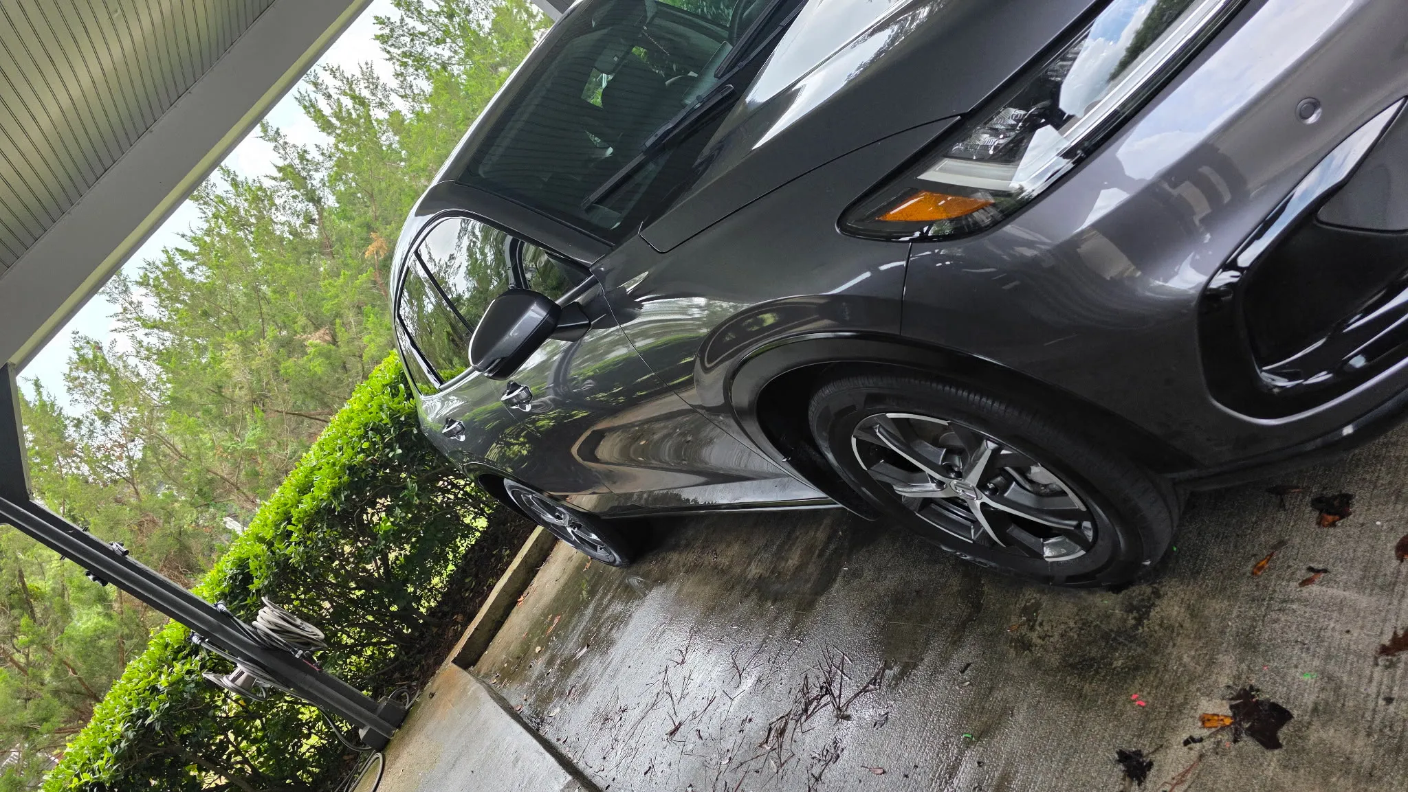 Side profile of a grey crossover on a wet driveway after washing