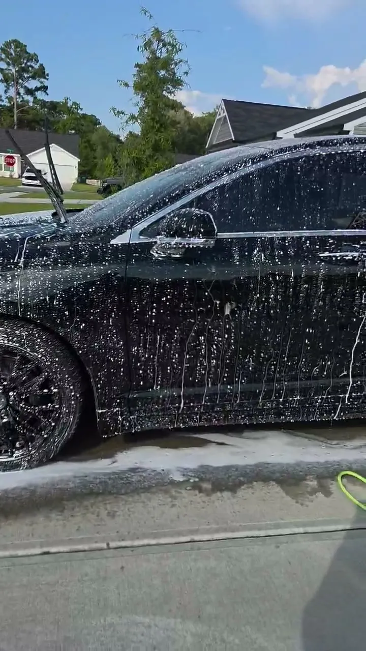 Thick foam running down the side and wheel of a black sedan during a hand wash
